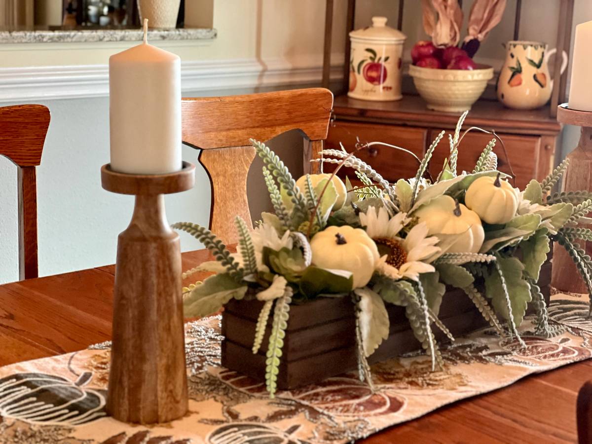 Close-up of adjustable track lighting heads illuminating layered seasonal home decor track lighting elements: woven pine boughs, matte-gold ornaments, and linen banners on a white-brick wall